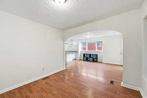 Unfurnished living room with light wood-style flooring, a textured ceiling, and arched walkways