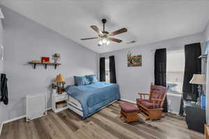 Bedroom with light wood-style flooring, a ceiling fan, and vaulted ceiling