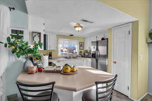 Kitchen featuring a peninsula, stainless steel refrigerator with ice dispenser, white cabinets, a textured ceiling, and a breakfast bar