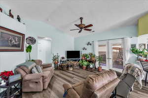Living room featuring french doors, vaulted ceiling, ceiling fan, wood finished floors, and a textured ceiling