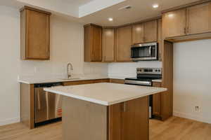 Kitchen with stainless steel appliances, brown cabinets, a kitchen island, light wood-type flooring, and recessed lighting