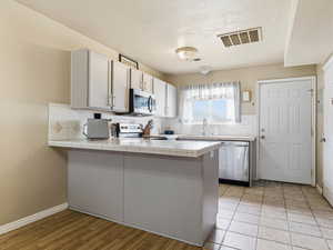 Kitchen featuring tile countertops, a peninsula, appliances with stainless steel finishes, tasteful backsplash, and a textured ceiling