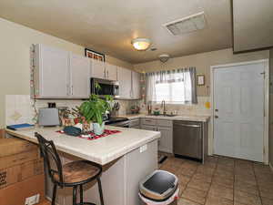 Kitchen featuring tile counters, stainless steel appliances, a peninsula, a kitchen breakfast bar, and backsplash