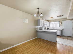 Kitchen with light countertops, a peninsula, hanging light fixtures, dishwasher, and backsplash