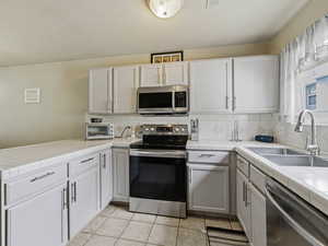 Kitchen with stainless steel appliances, tile counters, decorative backsplash, and a peninsula