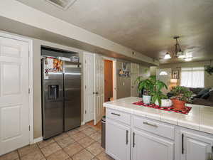 Kitchen with tile counters, stainless steel refrigerator with ice dispenser, open floor plan, and decorative light fixtures
