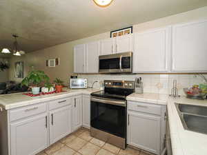 Kitchen featuring stainless steel appliances, a peninsula, tile counters, open floor plan, and tasteful backsplash