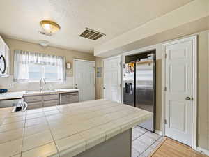 Kitchen featuring tile countertops, appliances with stainless steel finishes, a peninsula, a textured ceiling, and decorative backsplash