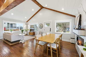Dining space with a fireplace, beamed ceiling, dark wood-style flooring, plenty of natural light, and high vaulted ceiling