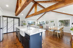 Kitchen featuring light stone counters, dark wood-type flooring, freestanding refrigerator, a kitchen island with sink, and a breakfast bar area