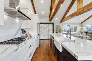 Kitchen featuring white cabinets, light stone counters, wall chimney exhaust hood, a spacious island, and recessed lighting