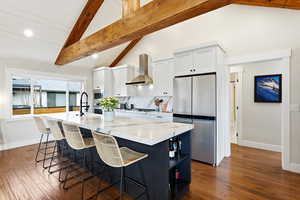 Kitchen with white cabinets, open shelves, appliances with stainless steel finishes, a breakfast bar area, and a center island with sink