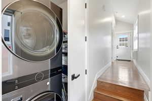 Laundry room featuring light wood-type flooring, stacked washing machine and dryer, and lofted ceiling
