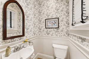 Half bath featuring wainscoting, wallpapered walls, and a decorative wall
