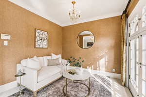 Living room featuring ornamental molding, a chandelier, and wallpapered walls