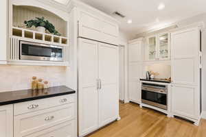Kitchen featuring dark countertops, built in appliances, glass insert cabinets, white cabinets, and recessed lighting