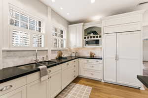 Kitchen with built in appliances, open shelves, light wood finished floors, tasteful backsplash, and white cabinetry