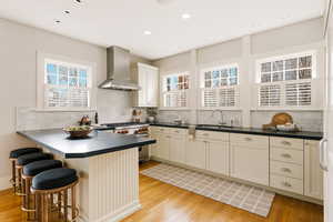Kitchen featuring dark countertops, light wood finished floors, wall chimney range hood, and recessed lighting