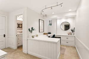 Office with built in desk, light carpet, and rail lighting