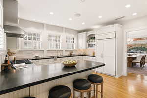 Kitchen featuring a breakfast bar, white cabinetry, built in appliances, and recessed lighting