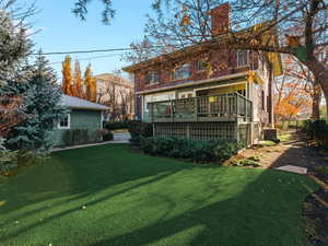 Rear view of house with a chimney, a yard, a deck, and an area to practice putting
