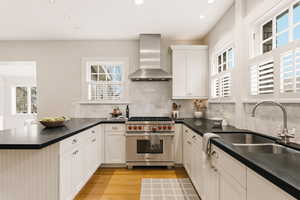 Kitchen featuring designer stove, wall chimney exhaust hood, a peninsula, light wood finished floors, and recessed lighting