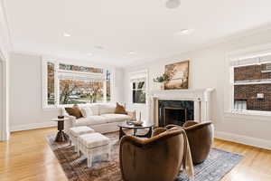 Living area with a premium fireplace, light wood-style flooring, ornamental molding, and recessed lighting