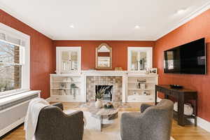 Living room with radiator heating unit, a tile fireplace, ornamental molding, light wood-type flooring, and recessed lighting