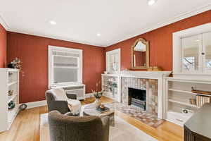 Living area with crown molding, a tiled fireplace, light wood-style flooring, radiator heating unit, and recessed lighting