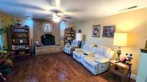 Living area with dark wood-type flooring, a brick fireplace, and ceiling fan