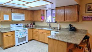 Kitchen with white appliances, light stone countertops, a kitchen breakfast bar, a peninsula, and light tile patterned flooring