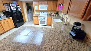 Kitchen featuring white appliances, light stone counters, separate washer and dryer room, and wood cabinets