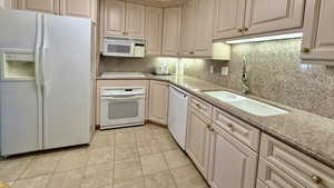 Kitchen featuring white appliances, backsplash, light stone counters, and light tile patterned flooring