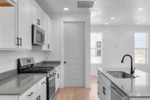 Kitchen with stainless steel appliances, recessed lighting, white cabinets, and light wood-style floors