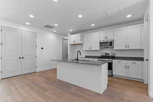 Kitchen featuring appliances with stainless steel finishes, white cabinets, dark countertops, recessed lighting, and light wood-type flooring