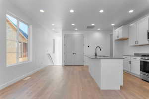 Kitchen featuring white cabinetry, recessed lighting, light wood-style floors, stainless steel gas range, and a center island with sink