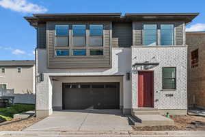 Contemporary home featuring an attached garage, driveway, and brick siding