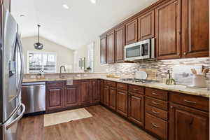 Kitchen featuring stainless steel appliances, lofted ceiling, light stone counters, dark wood finished floors, and decorative backsplash