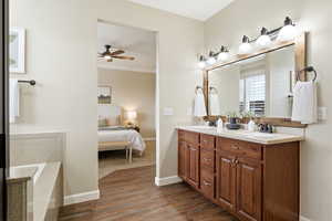 Ensuite bathroom with double vanity, dark wood-type flooring, a tub, crown molding, and ceiling fan