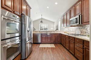 Kitchen featuring appliances with stainless steel finishes, vaulted ceiling, pendant lighting, dark wood-style floors, and light stone countertops