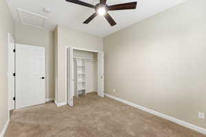 Unfurnished bedroom with attic access, light carpet, ceiling fan, and a closet