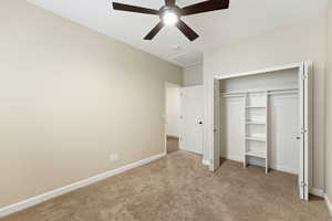Unfurnished bedroom with attic access, light colored carpet, a closet, and ceiling fan