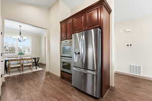 Kitchen featuring appliances with stainless steel finishes, a chandelier, hanging light fixtures, ornamental molding, and dark wood-style floors