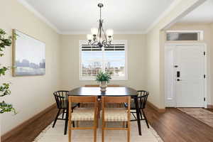 Dining space with wood finished floors, crown molding, and a chandelier