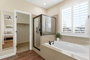 Full bath featuring dark wood-style floors, a stall shower, a bath, and a walk in closet