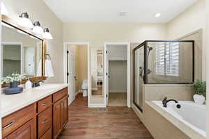 Full bath with a walk in closet, double vanity, a shower stall, dark wood-style floors, and a garden tub