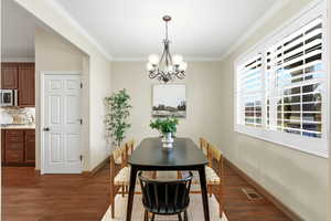 Dining room with dark wood finished floors, ornamental molding, and a chandelier