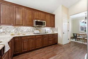 Kitchen featuring stainless steel microwave, decorative light fixtures, a chandelier, light stone countertops, and vaulted ceiling