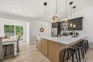 Kitchen featuring a peninsula, a ceiling fan, light wood finished floors, appliances with stainless steel finishes, and a kitchen bar