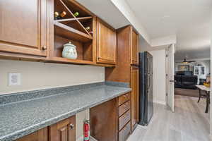 Kitchen featuring light wood-type flooring, freestanding refrigerator, open shelves, brown cabinetry, and a ceiling fan